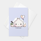 Front view of a greeting card featuring an original illustration of a smiling bulb of garlic holding the string of a heart-shaped balloon shaped like two garlic cloves. To the left of the bulb, additional cloves of garlic and two purple flowers. Text beneath the bulb of garlic reads “I clove you.”